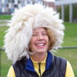 Nancy Gell smiles while wearing a hat that looks like white, poofy hair