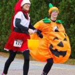 A runner in a pumpkin costume runs alongside a friend
