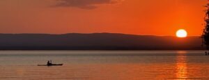 Cathy kayaking on the lake at sunset against a smoldering orange sky